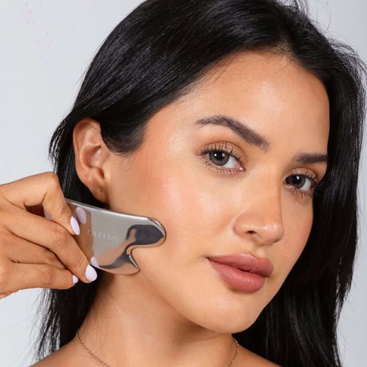 Gua sha UAE – Delune Dubai Stainless Steel Gua Sha used along a woman's cheek