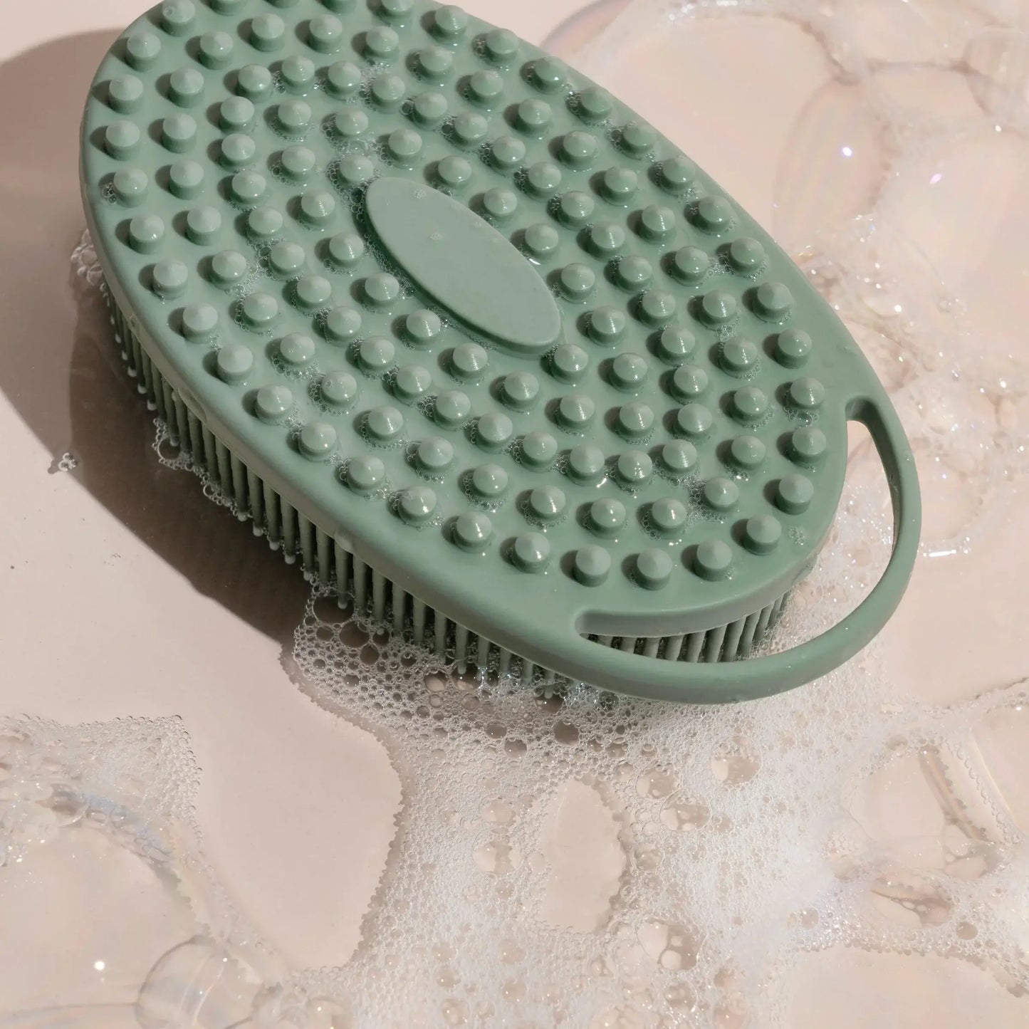 Green silicone body scrubber with gentle bristles and ergonomic handle, surrounded by suds, designed for effective cleaning and massage.