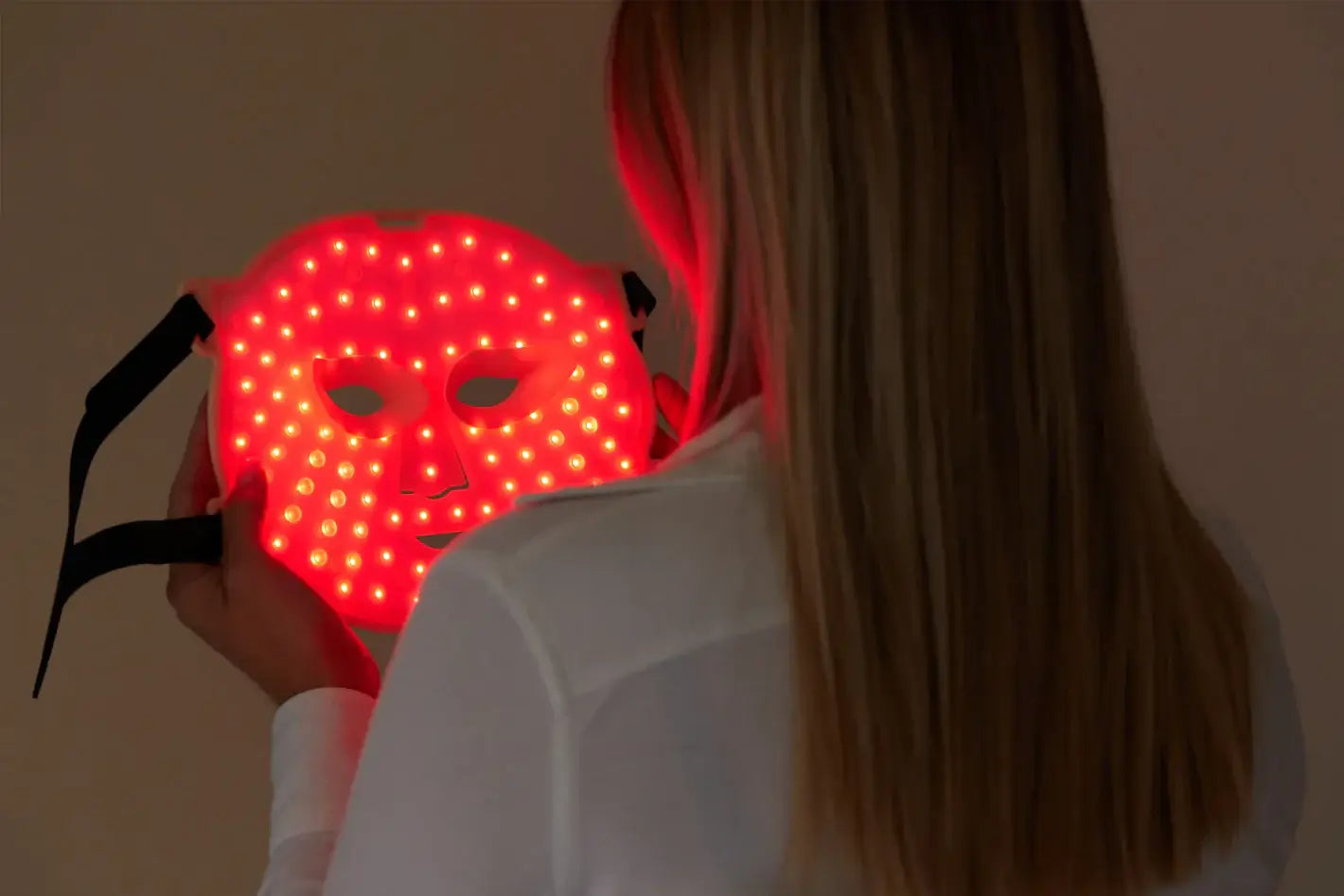 Woman holding Delune Beauty's red LED light therapy mask for anti-aging facial treatment.