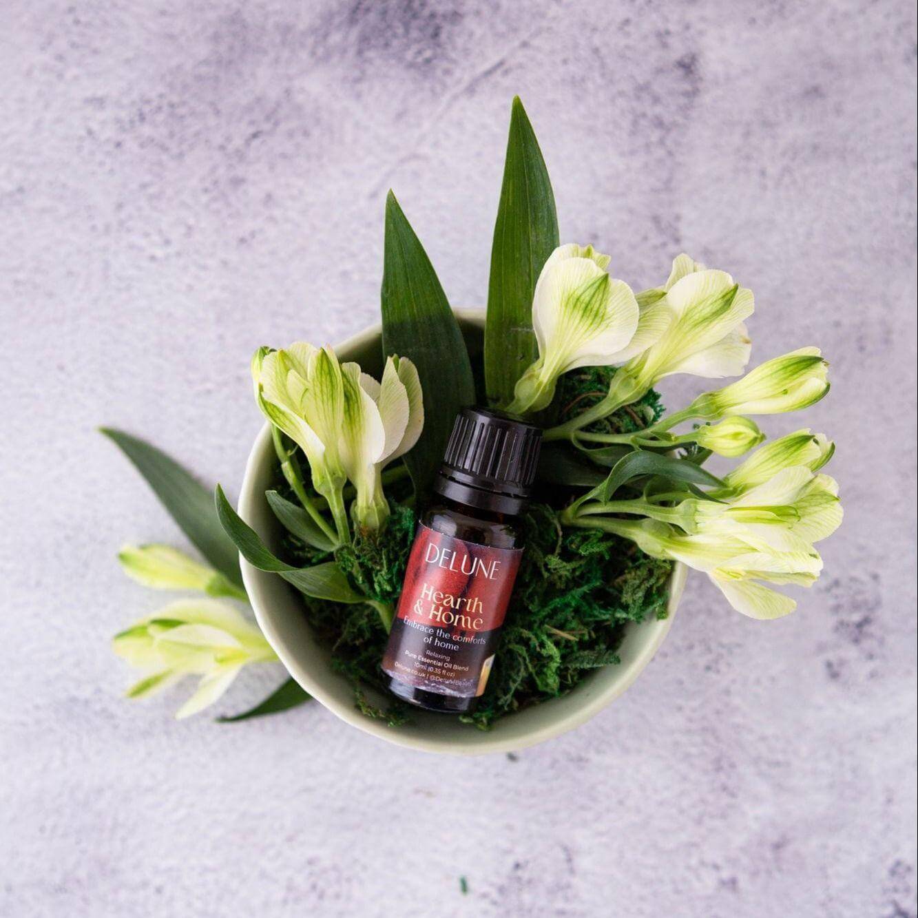 Hearth & Home essential oil blend bottle surrounded by fresh flowers, capturing the cozy and comforting aroma of cinnamon, clove, and vanilla.
