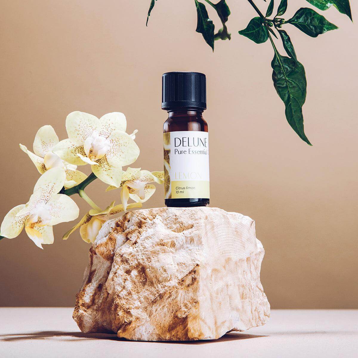 Lemon Pure Essential Oil bottle on a rock, surrounded by flowers and greenery, highlighting its fresh, citrusy, and uplifting scent.