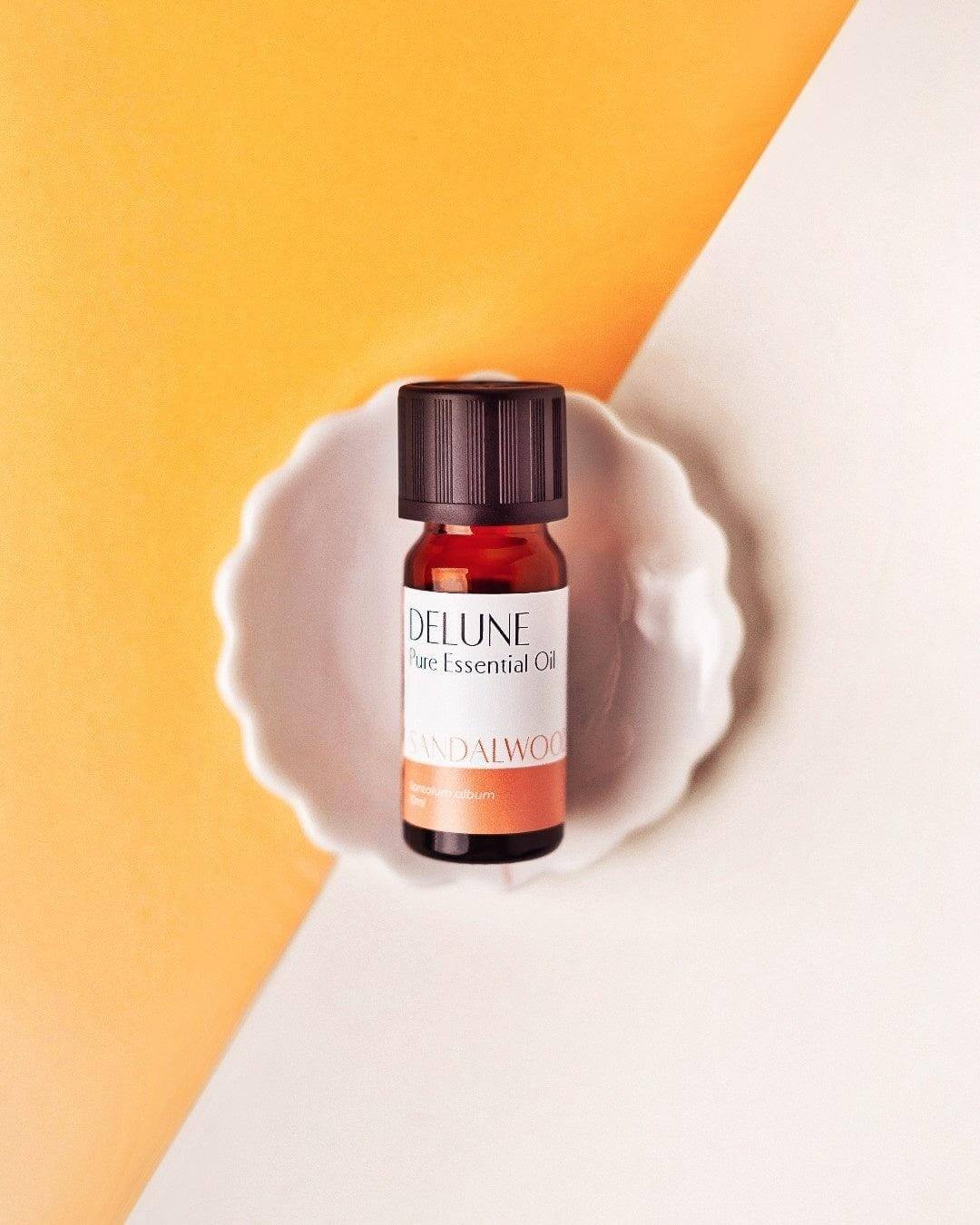 Bottle of Sandalwood Pure Essential Oil for relaxation and skincare, placed on a white dish against a yellow and white background.