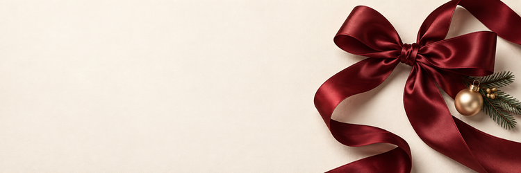 Burgundy satin ribbon and a gold Christmas ornament on warm ivory