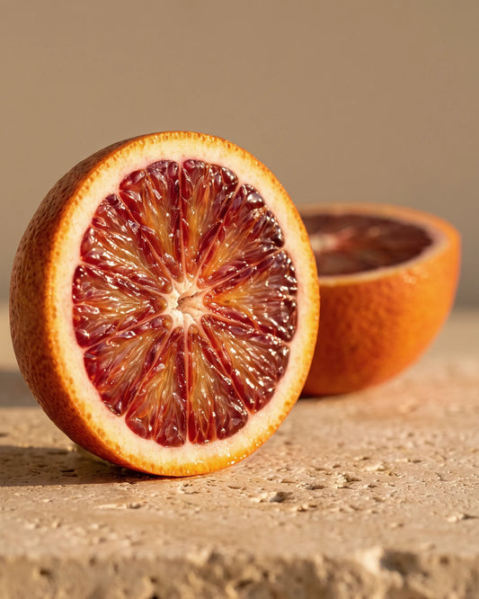 Blood Orange essential oil UAE – Delune Dubai: a halved blood orange with deep ruby flesh on warm travertine