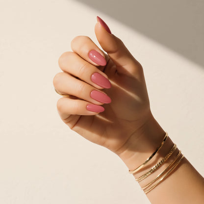 Nail wraps UAE – Hand wearing Delune Dubai Blush mauve-pink nail wraps with gold bangles against a warm plaster wall