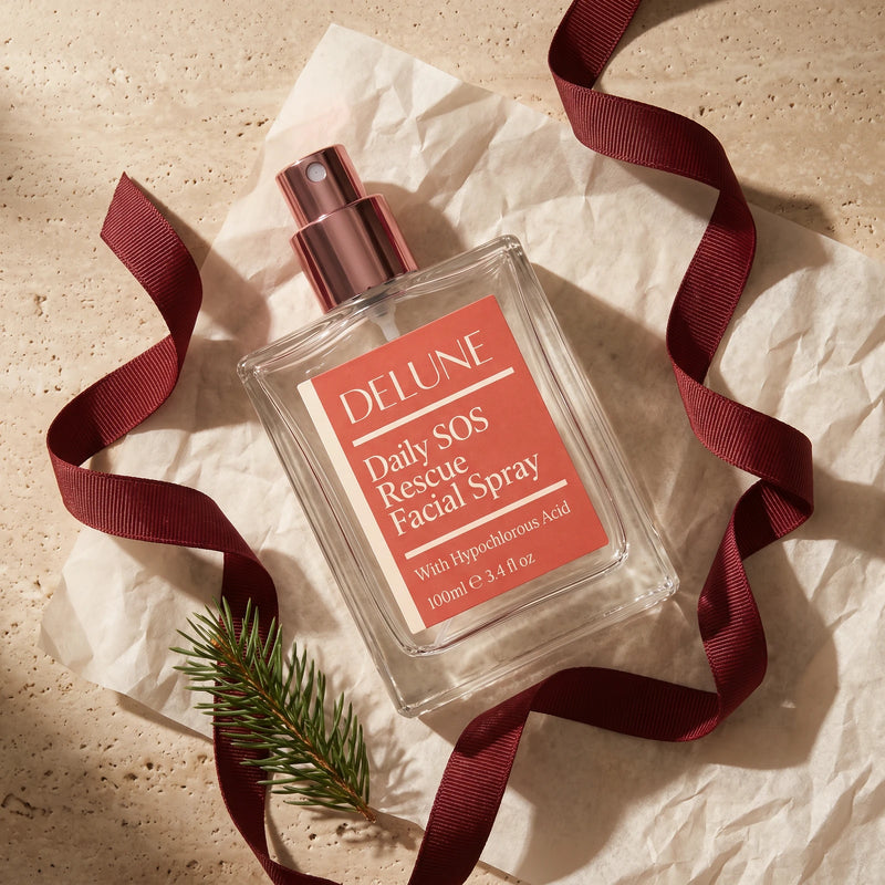 Daily SOS Rescue Facial Spray lying on tissue paper with a curling oxblood ribbon and a sprig of pine