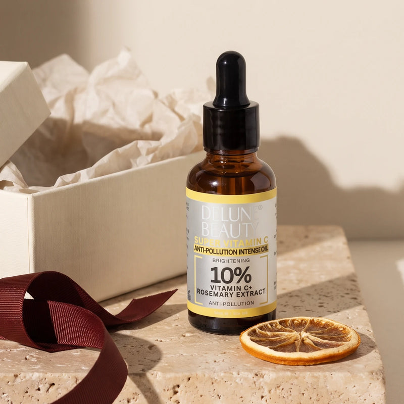 Super Vitamin C Brightening Oil on travertine beside an open gift box, oxblood ribbon and a dried orange slice in warm sunlight