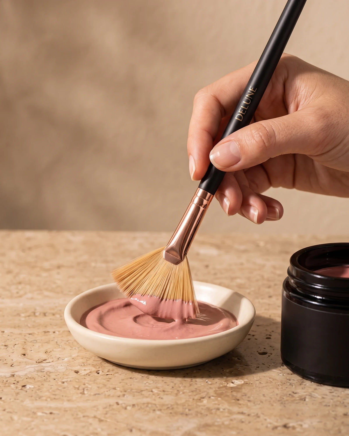 Facial tool UAE – Hand loading the Delune Dubai fan brush with rose clay paste from a ceramic dish