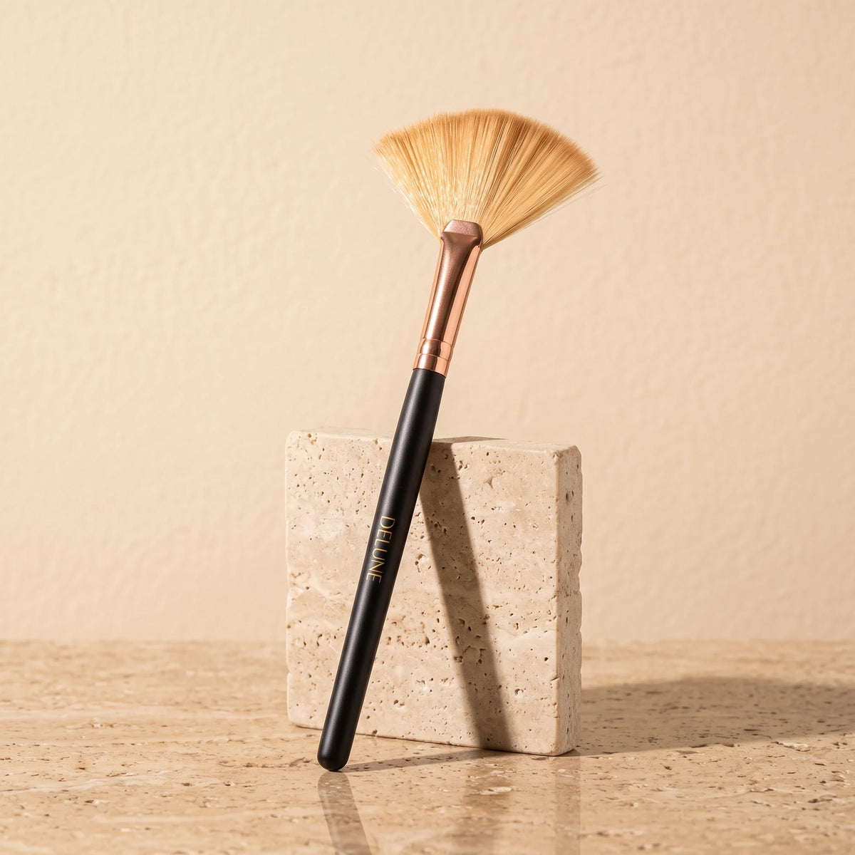 Facial tool UAE – Delune Dubai clay mask fan brush with rose-gold ferrule leaning on a travertine block