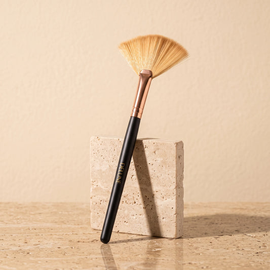 Facial tool UAE – Delune Dubai clay mask fan brush with rose-gold ferrule leaning on a travertine block