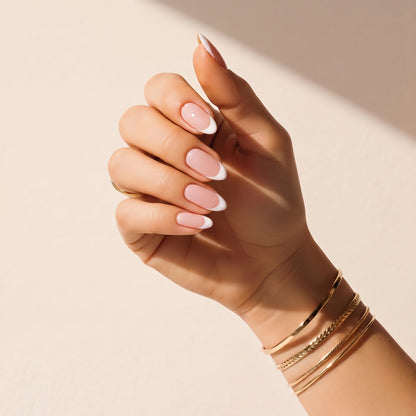 Nail wraps UAE – Hand wearing Delune Dubai French Manicure nail wraps with gold bangles against a warm plaster wall