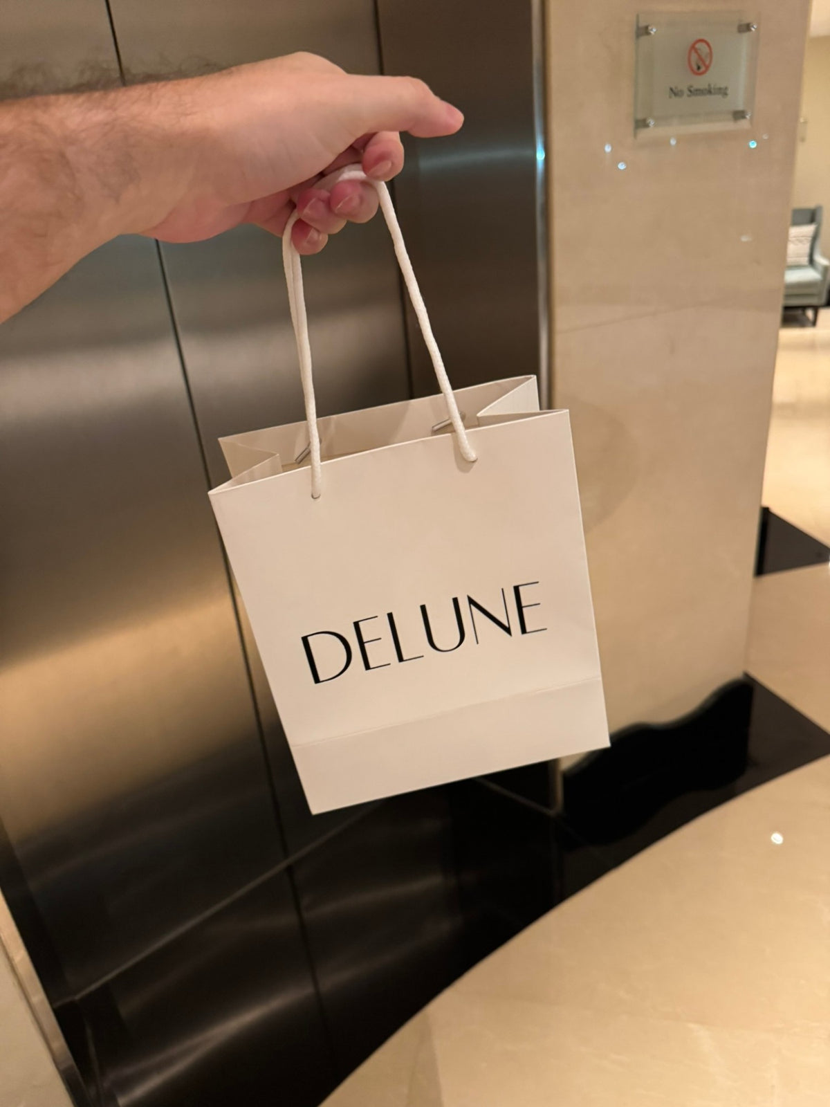 A hand holding a white Delune gift bag, on the way to deliver an order