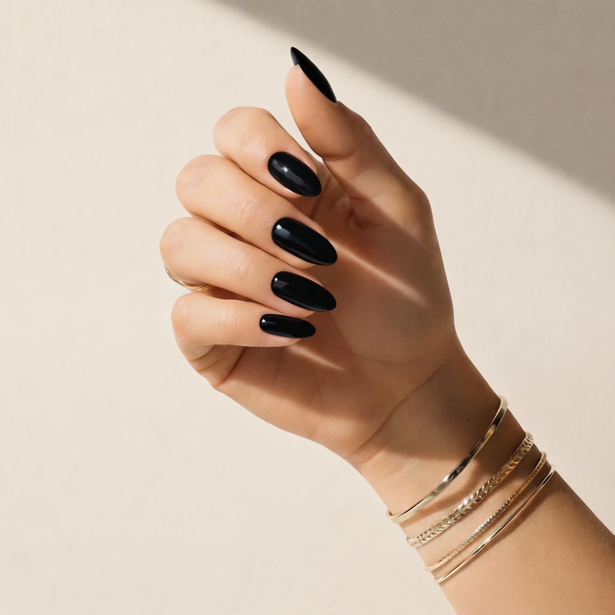 Nail wraps UAE – Hand wearing Delune Dubai Noir glossy black nail wraps with gold bangles against a warm plaster wall