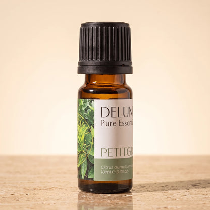 Delune Petitgrain Pure Essential Oil, 10ml amber glass bottle on warm travertine stone