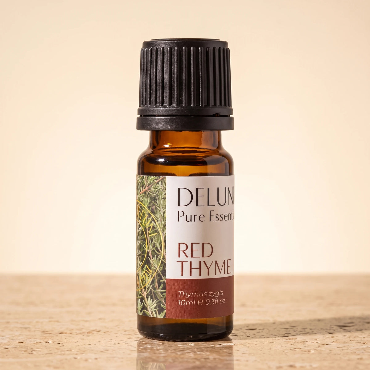 Delune Red Thyme Pure Essential Oil, 10ml amber glass bottle on warm travertine stone
