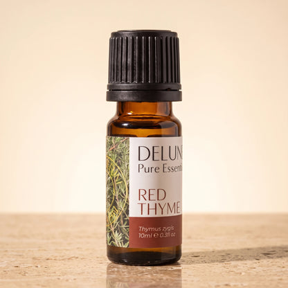 Delune Red Thyme Pure Essential Oil, 10ml amber glass bottle on warm travertine stone