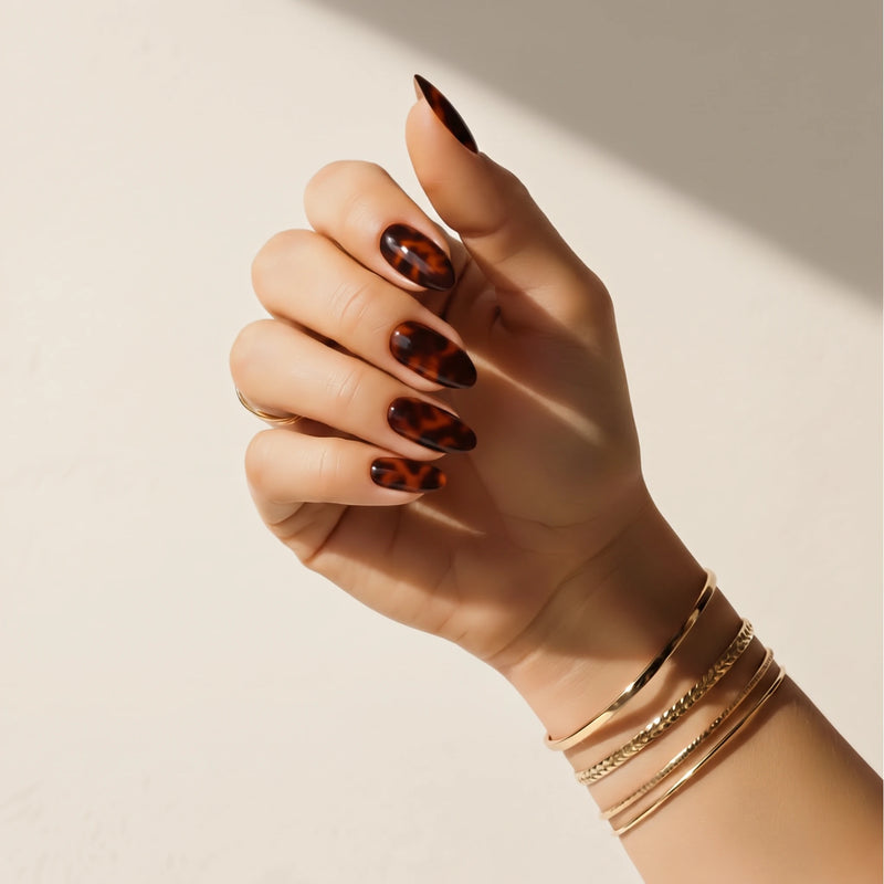 Nail wraps UAE – Hand wearing Delune Dubai Tortoiseshell nail wraps with gold bangles against a warm plaster wall