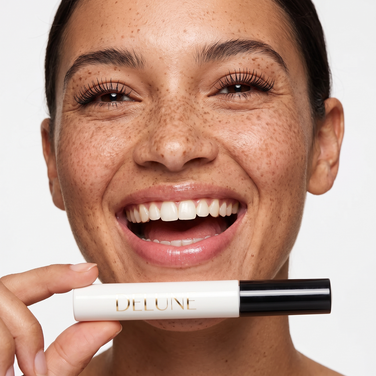 Model laughing with lifted lashes, holding Delune Dubai Tubing Mascara